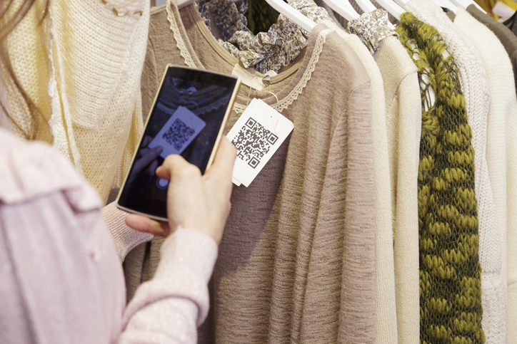 Woman scanning a QR code, with her smart phone, from a label in a clothing store. No face.